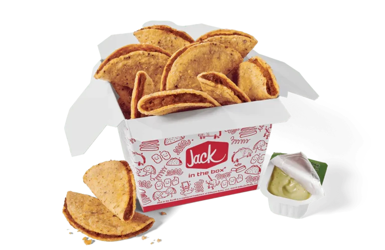 A box of Tiny Tacos from Jack in the Box. The tacos are packed in a white box decorated with red illustrations and the Jack in the Box logo. The tacos have crispy shells and are filled with seasoned meat. Some tacos are displayed outside the box for emphasis. A small dipping cup with partially opened lid, filled with green avocado lime sauce, is included on the side. The image has a transparent background.